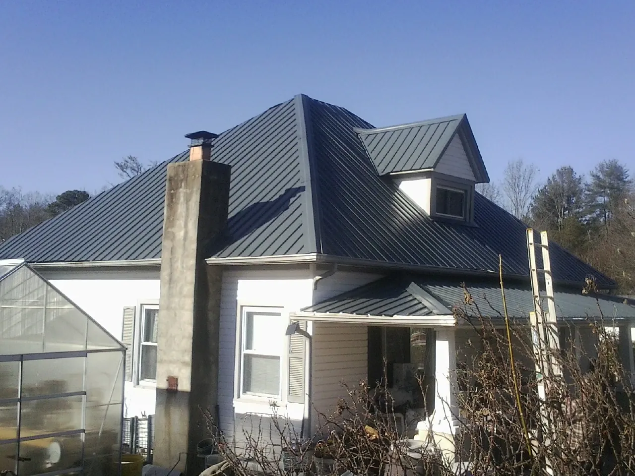 Dark blue standing seam metal roof on a white farmhouse with dormer — Slate & Tile Roof Repair by Roofing Brothers in White Bluff