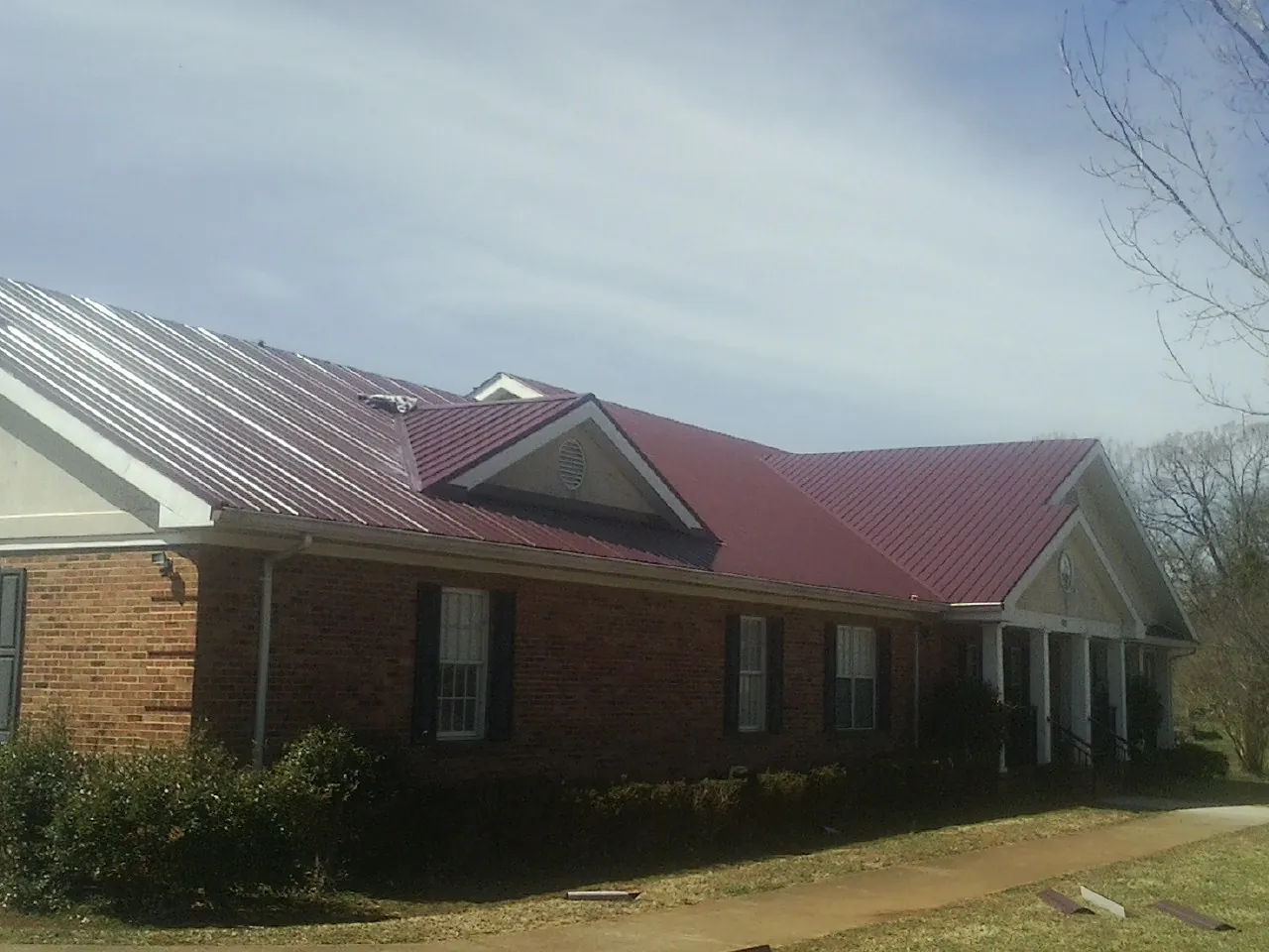 Red metal roof with gabled entries on a long brick building, from a Hail Damage Roof Repair job in White Bluff