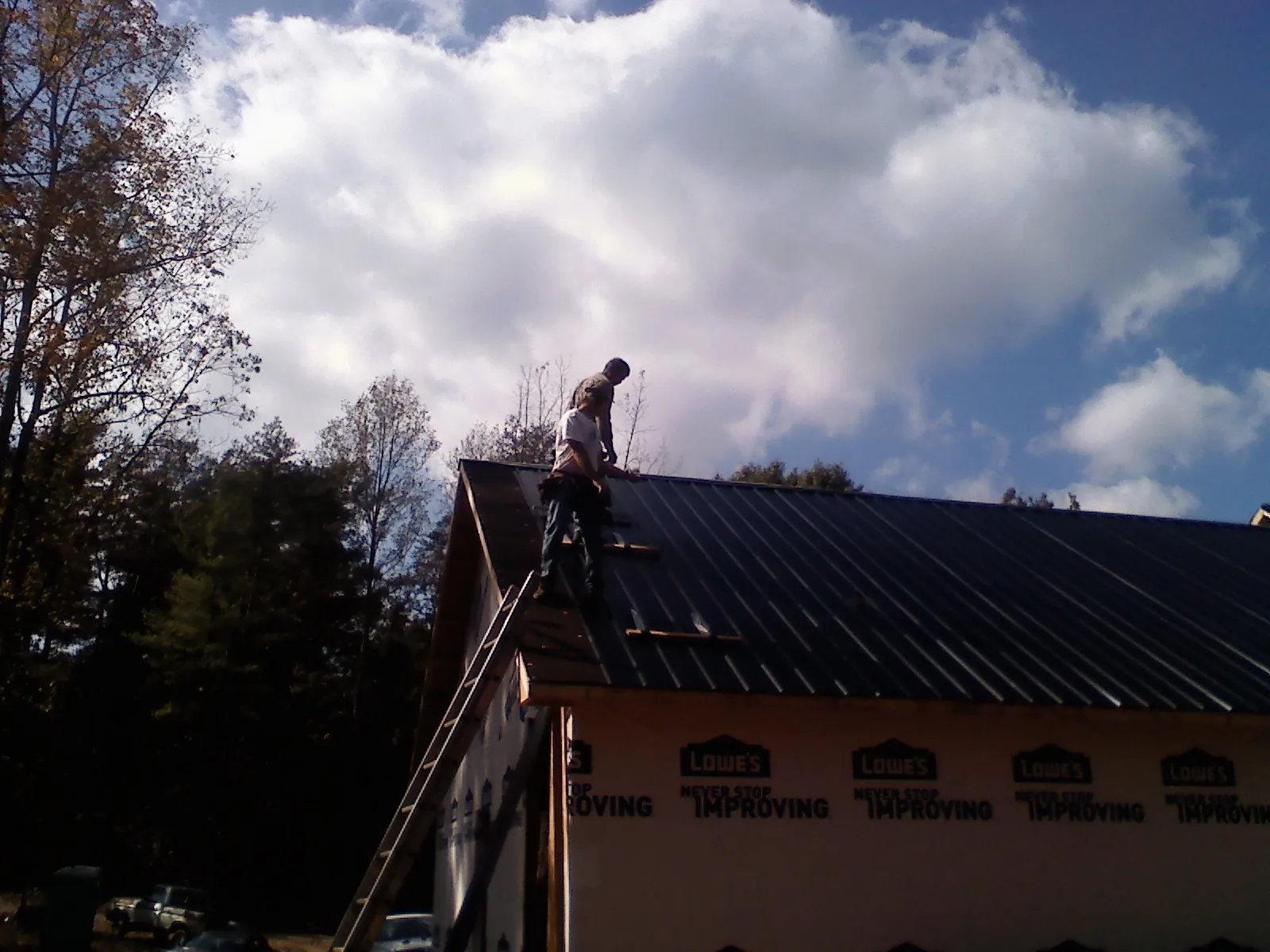 Roofer fastening dark metal panels high against a cloudy sky, from a Roof Inspection job in White Bluff