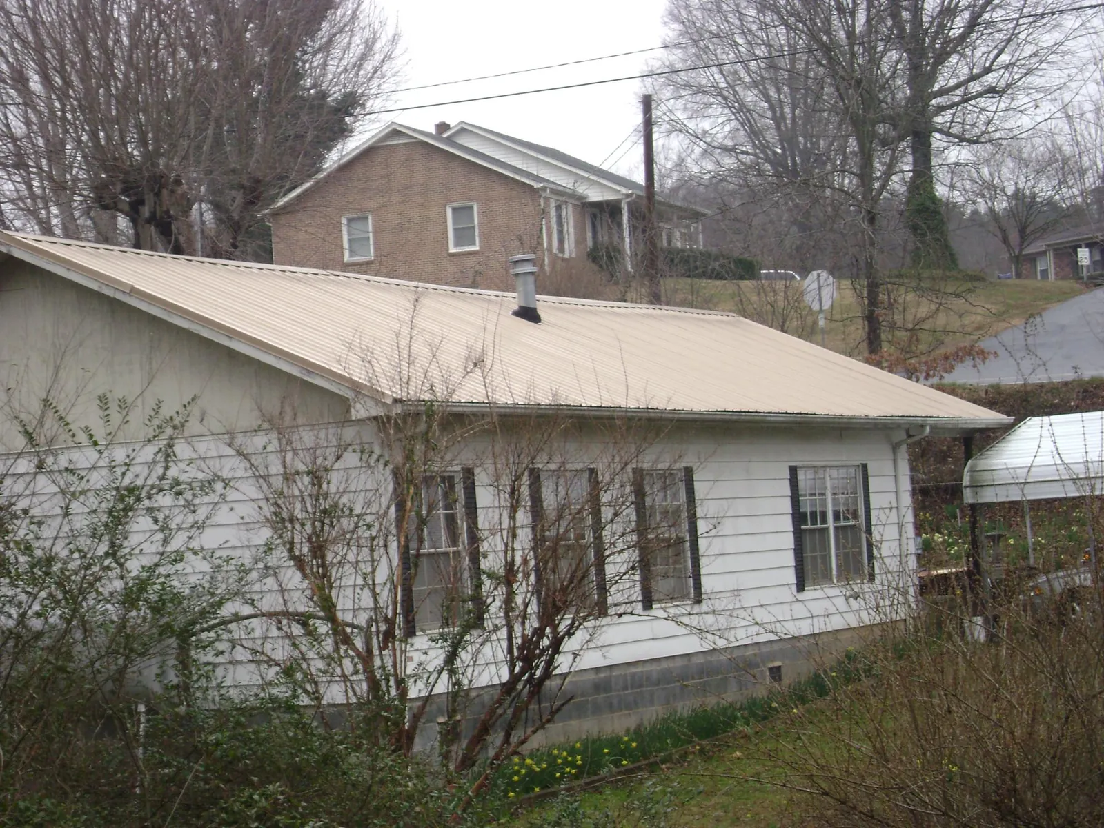 Tan metal roof on a white sided house set into a hillside — Commercial Roofing by Roofing Brothers in White Bluff