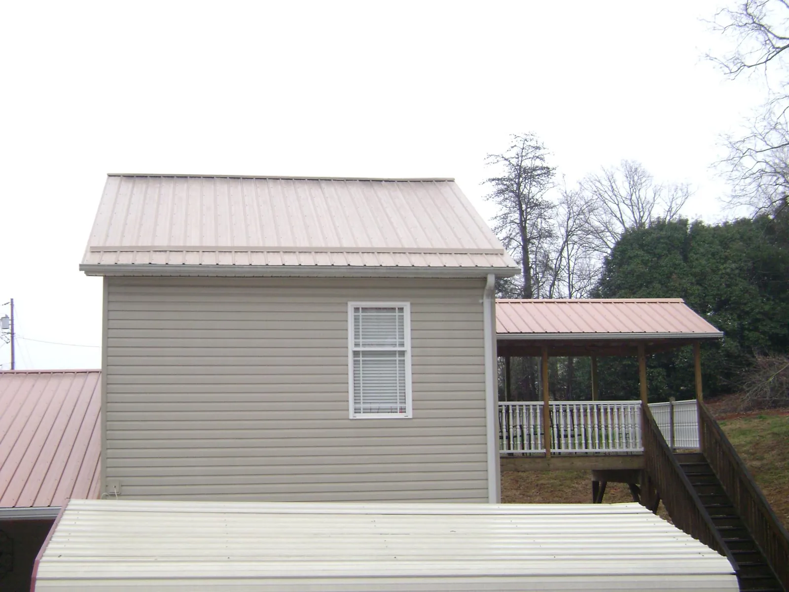 Tan metal roofs on a two story addition and attached porch, from a Roof Replacement job in White Bluff